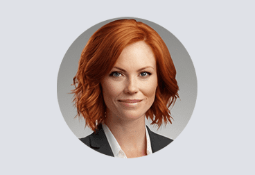 face of female freelancer with red hair wearing a gray jacket over a white shirt